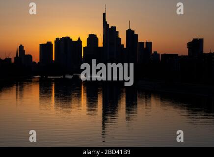 06 aprile 2020, Hessen, Francoforte sul meno: Lo skyline scuro delle banche di Francoforte si riflette nelle acque del meno. Nonostante le temperature primaverili, le strade e i ponti della città non sono molto affollati a causa delle restrizioni al movimento causate dalla pandemia della corona. Foto: Boris Roessler/dpa Foto Stock