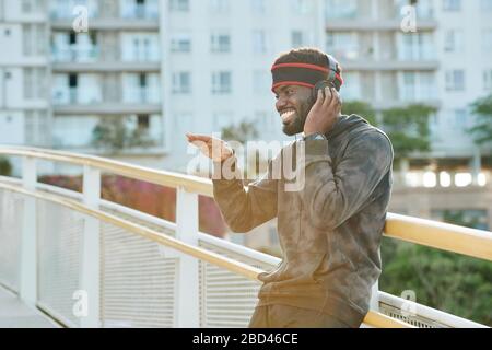 Felice bel giovane uomo in piedi per strada e quasi ballare alla musica in cuffie Foto Stock