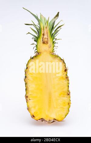 ananas tagliato a metà isolato di fronte a uno sfondo bianco. Il cuore giallo della frutta è succoso e colorato con foglie verdi Foto Stock