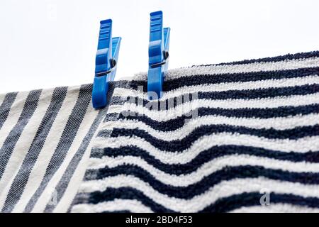Panni per stoviglie che si asciugano sulla linea di abbigliamento. Primo piano di due asciugamani a righe orizzontali e verticali grigi bianchi neri che asciugano su una linea con due teli blu. Foto Stock