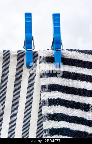 Panni per stoviglie che si asciugano sulla linea di abbigliamento. Primo piano di due asciugamani a righe orizzontali e verticali grigi bianchi neri che asciugano su una linea con due teli blu. Foto Stock