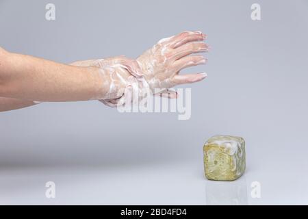 Le mani bianche si lavano con il sapone verde schiumoso di Marsiglia isolato di fronte a uno sfondo grigio con luci e ombre strutturanti Foto Stock
