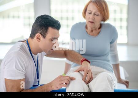 Fisioterapista professionista esperto che controlla il ginocchio dei suoi pazienti Foto Stock