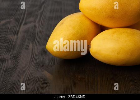 Quattro manga di frutta intera su tavola di legno. Grandi e succulenti frutti gialli maturi su sfondo scuro Foto Stock