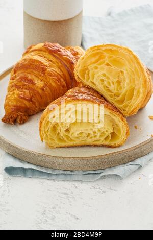 Due deliziosi croissant sul piatto e una bevanda calda nella tazza. Vista in sezione del croissant, Foto Stock