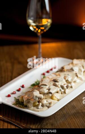 Carne di pollo su gnocchi grattugiati in salsa di funghi e formaggio affumicato in tavola con bicchiere di vino bianco Foto Stock