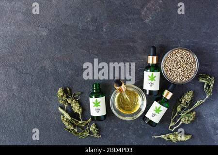 Bottiglie verdi di olio medico CBD con semi di cannabis e foglie secche vista dall'alto su sfondo nero. Estratto di cannabis medica. Medicina alternativa Foto Stock