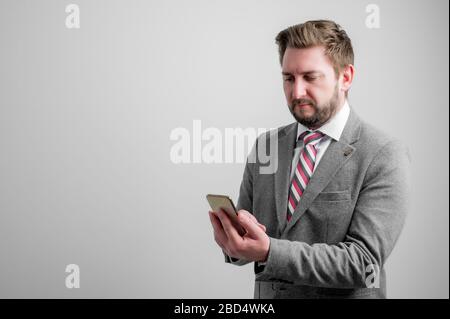 Ritratto di uomo d'affari che indossa abiti da lavoro utilizzando applicazioni mobili che testano su cellulare isolato su sfondo grigio con spazio copia pubblicità Foto Stock