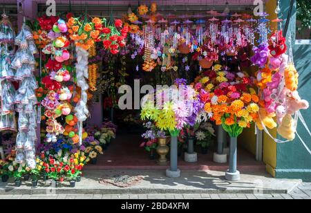 Una colorata esposizione di fiori di plastica e giocattoli morbidi in vendita in un negozio al di fuori dello Sri Lankathilaka Rajamaha Viharaya a Rabbegamuwa in Sri Lanka. Foto Stock