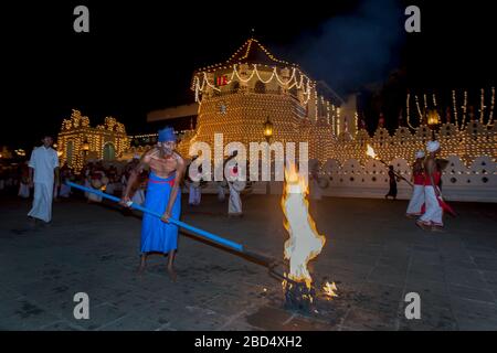 Un portatore di torce appoggia il suo fuoco ardente di bucce di cocco sul terreno di fronte al Tempio della Relica del dente Sacro a Kandy in Sri Lanka. Foto Stock