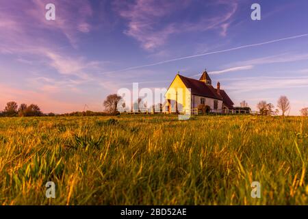 La Chiesa isolata di St Hubert, circondata da campi sul Parco Nazionale di South Downs, mentre il sole comincia a tramontare durante l'ora d'oro Foto Stock