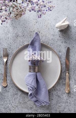 Tavolo di Pasqua con piatto grigio e decorazioni lilla su tavolo in pietra grigia. Cena elegante. Vista dall'alto. Formato verticale. Foto Stock