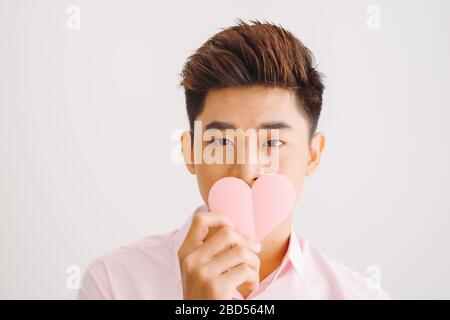 Bel giovane uomo asiatico legge biglietto di auguri a forma di cuore su sfondo bianco Foto Stock