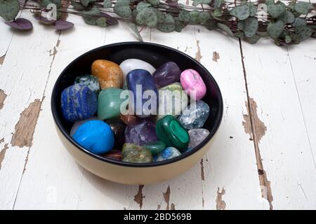 Una ciotola di gemme assortite fotografata contro una superficie bianca rustica Foto Stock