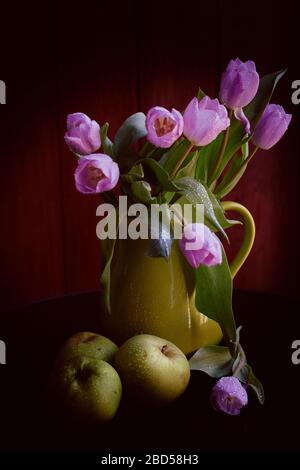 Un bouquet di tulipani lilla in un vaso verde con mele verdi ricoperte di gocce di pioggia su fondo nero Foto Stock