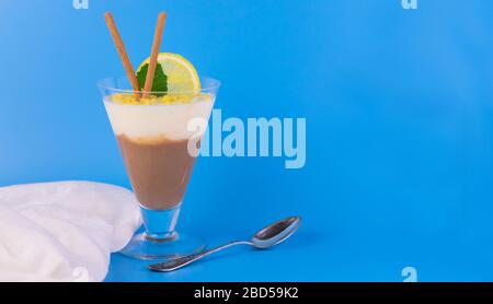 Budino di vaniglia al cioccolato in un bicchiere su sfondo azzurro. Spazio di copia. Foto Stock