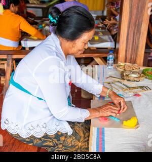 Ritratto quadrato di una signora che fa decorazioni religiose con pasta di riso in un tempio a Bali, Indonesia. Foto Stock