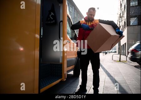 Gelsenkirchen, Germania. 7 aprile 2020. Nino Molldmann, il servizio di consegna pacchi di DHL, carica i pacchi dalla sua auto e li scansiona. È uno degli "eroi della crisi corona" e lavora in una professione di importanza sistemica. Credit: Fabian Strauch/dpa/Alamy Live News Foto Stock