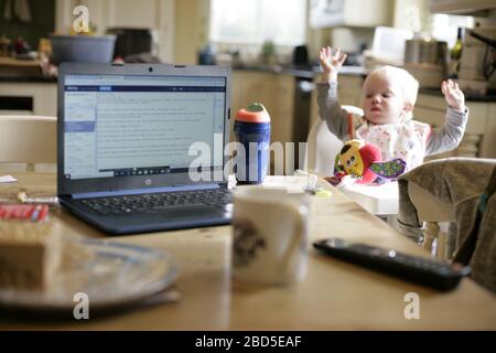 Madre che alimenta i suoi figli cena al tavolo da cucina mentre lavora da casa durante il periodo di autoisolamento - 2020 COVID-19 coronavirus pandemic Foto Stock