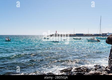 Piccole barche sull'oceano vicino a Playa Blanca, terminal dei traghetti di Lanzarote contro il cielo blu brillante Foto Stock