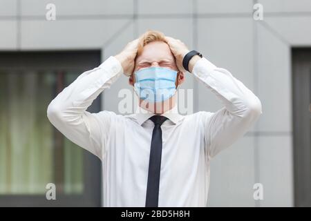 Concetto di emozioni e sentimenti cattivi. Mal di testa. Uomo d'affari con maschera medica chirurgica che tocca la testa e ha un problema di emicrania o di lavoro. Ssh. Outdoor Foto Stock