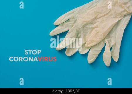 vista ad angolo elevato di un paio di guanti chirurgici monouso e del coronavirus di arresto del testo su uno sfondo blu Foto Stock