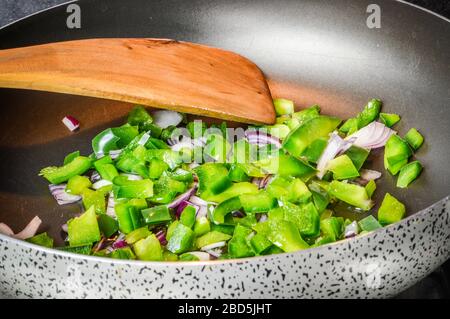Cottura a fette di cipolle e peperoni verdi su una padella da vicino. Foto Stock