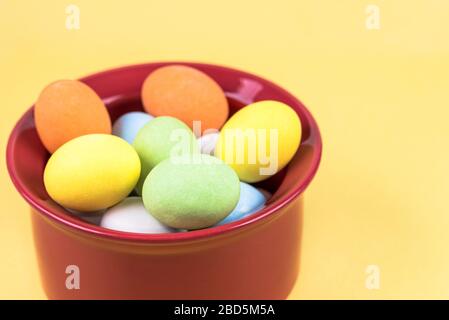 Piccole uova di Pasqua colorate in una tazza rossa su sfondo giallo. Spazio di copia. Foto Stock