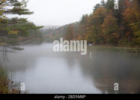 Bel fiume attraverso un paesaggio collinare boschivo durante la pioggia pesante in autum. Un'auto solitaria è visibile su una strada di riva del fiume. Foto Stock