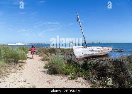 Vecchia barca abbandonata in baracche con camminatore sul sentiero costiero, Quinta de Marim, Parco Naturale Ria Formosa, Algarve, Portogallo Foto Stock