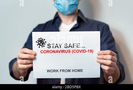 Man in Mask Holding Paper con Coronavirus Warning, sfondo grigio Foto Stock