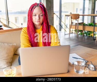 Concetto di nomade digitale. Ragazza freelancer a distanza che lavora sul laptop in bar, coworking. Foto Stock