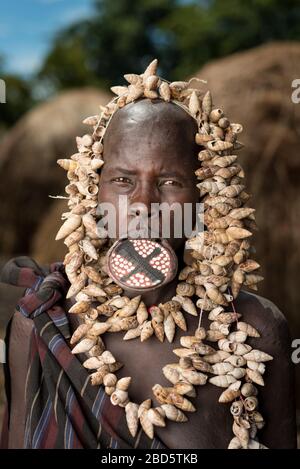 Con il suo piatto di labbra in argilla e collana di conchiglie, donna della tribù Mursi o gruppo etnico, villaggio Olikoru, Jenka, Etiopia. Foto Stock