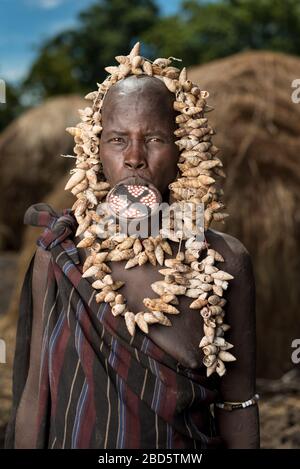 Con il suo piatto di labbra in argilla e collana di conchiglie, donna della tribù Mursi o gruppo etnico, villaggio Olikoru, Jenka, Etiopia. Foto Stock