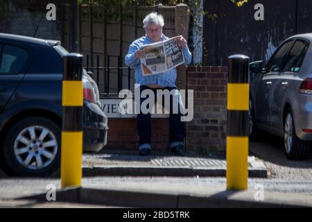 Manor Park, Londra, Regno Unito. 7 aprile 2020. Un uomo legge un giornale che il titolo dice: 'PM messo a unità di cura intesive', vicino al morgue.Works sulla costruzione di un morgue temporaneo a Manor Park, Londra est continua; a causa di focolaio di coronavirus. Credit: Marcin Nowak/Alamy Live News Foto Stock