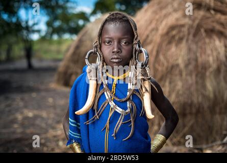 Una giovane ragazza si adorna di corno di bestiame, pelletteria e gioielli in metallo, tribù Mursi o gruppo etnico, Olikoru Village, Jenka, Etiopia. Foto Stock