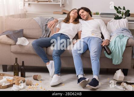 Dopo la festa. Una giovane coppia dorme ubriaco sul divano in una camera caotica Foto Stock