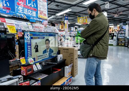 Una donna guarda una TV in un negozio elettronico mentre il primo ministro giapponese Shinzo Abe parla a una conferenza stampa e rivolgendosi al cittadino attraverso la TV.il primo ministro Shinzo Abhas ha dichiarato che il Giappone è in stato di emergenza, in quanto le riunioni sociali non essenziali saranno vietate e i residenti sono Richiesto di autoisolare poiché il coronavirus COVID-19 continua a diffondersi. Foto Stock