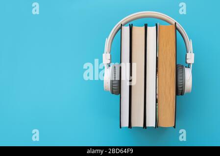 Cuffie bianche con una pila di libri su sfondo blu. Libri audio o concetto di istruzione moderna Foto Stock