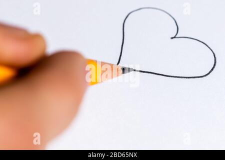 Immagine macro della punta di una matita nel processo di disegno di un cuore su carta bianca. Ampio spazio per la scrittura di copie sulla superficie della carta bianca e. Foto Stock