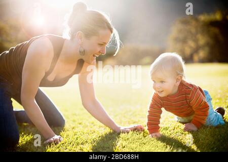 La giovane madre e il suo figlio piccolo strisciano su un prato. Foto Stock