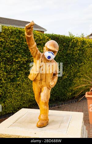 Statua "Clockpelter" con maschera medica durante la pandemia del virus Corona Covid-19. Great Gonerby, Grantham, Lincolnshire, Inghilterra. Aprile 2020 Foto Stock