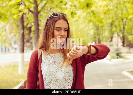 Donna felice sorridente guardando il orologio da polso isolato su sfondo verde parco Foto Stock