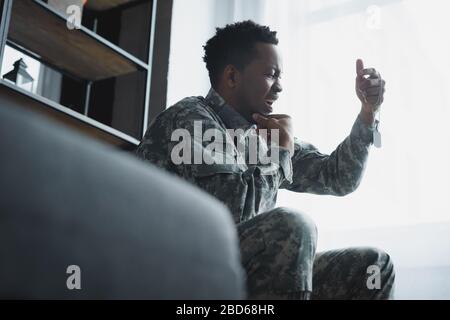 Stressato soldato africano americano piangendo e tenendo in mano il badge dell'esercito a casa, che soffre di PTSD Foto Stock
