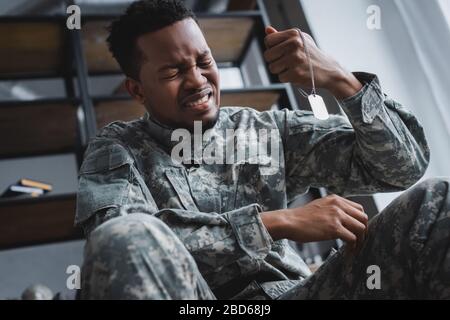 Piangendo soldato afro-americano che tiene il badge dell'esercito a casa, soffrendo di PTSD Foto Stock