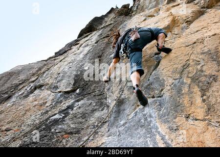 L'uomo che raggiunge la mano successiva tiene mentre si arrampica su roccia. Foto Stock