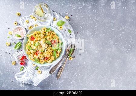 Ravioli italiani, tortellini con parmigiano e verdure - spinaci, pomodori, funghi e basilico, su sfondo in pietra grigia Foto Stock