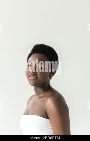 attraente ragazza afro-americana sorridente in bianco top isolato su grigio Foto Stock