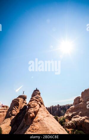 Un uomo che salta per la gioia sopra una pinna di arenaria nel Parco Nazionale di Arches mentre il suo amico scatta la sua foto. Utah, Stati Uniti. Foto Stock