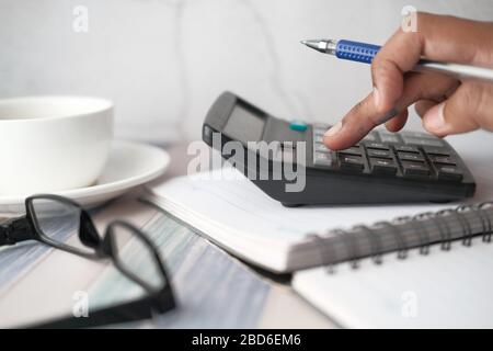 Primo piano della mano dell'uomo usando la calcolatrice e la tabella finanziaria sul tavolo Foto Stock